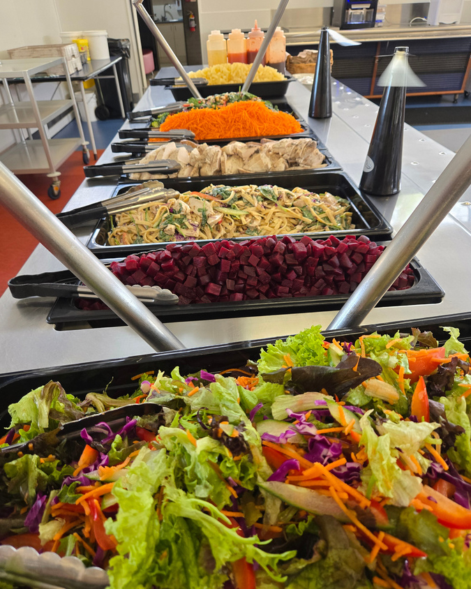 Selection of freshly made salad, sausage, grilled chicken, vegetables, and fruits.